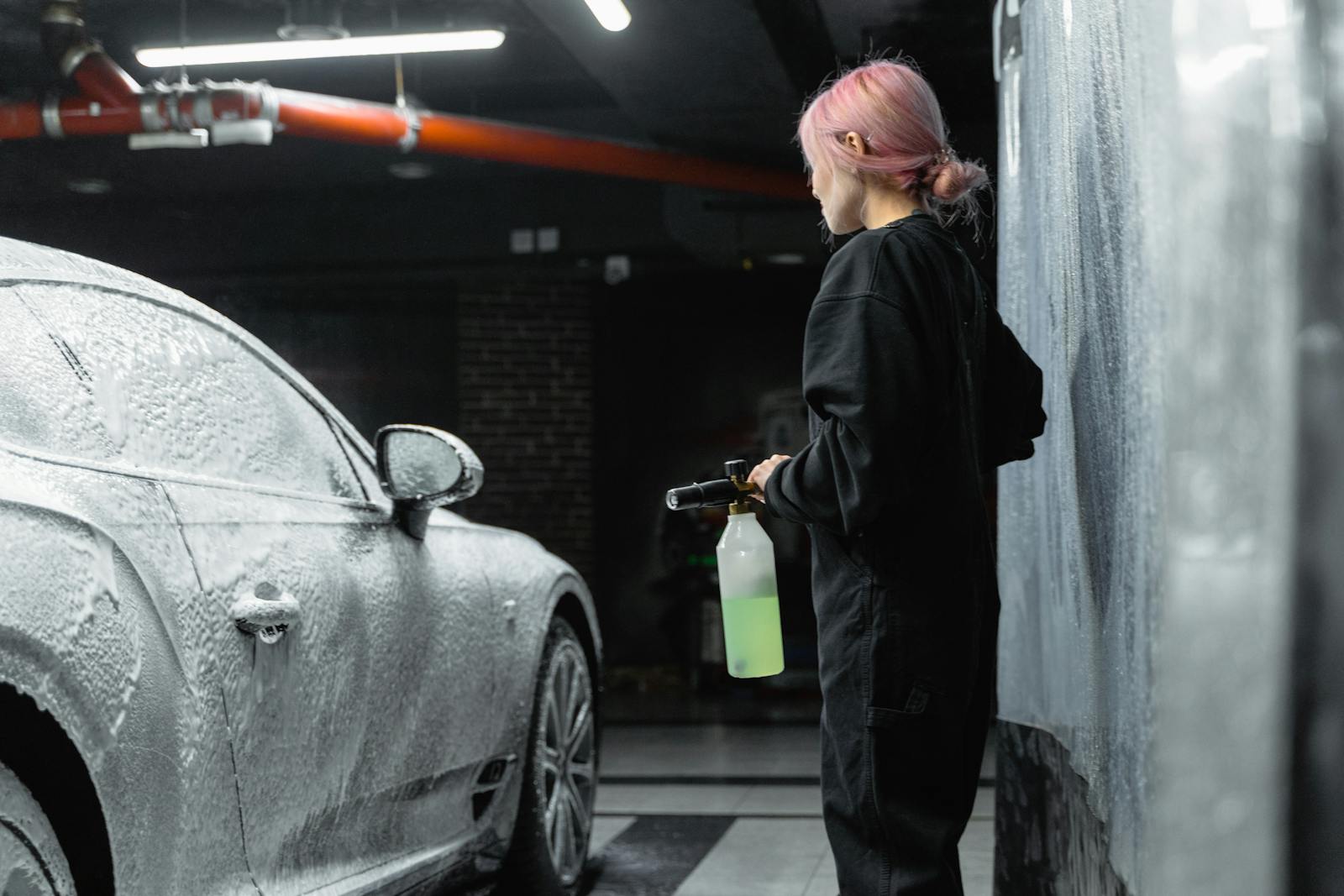 Young woman washing a car with foam in an indoor garage setting, showcasing car care and maintenance.